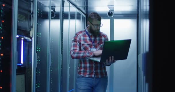 Bearded IT engineer using laptop in server room - Footage, Video