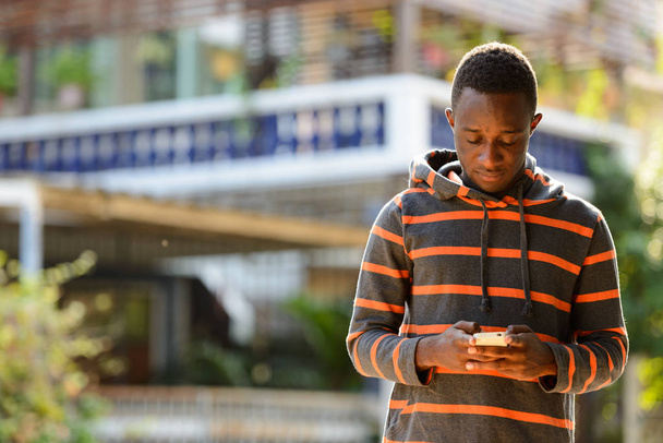 Молодой человек из Африки использует мобильный телефон на открытом воздухе  - Фото, изображение