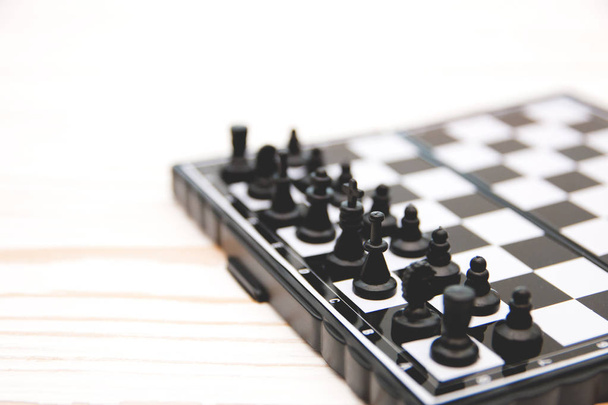 small pocket chess, plastic chess pieces placed on a chessboard on a white wooden background - Foto, imagen