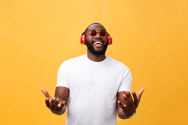 Guapo joven afroamericano escuchando y sonriendo con música en su dispositivo móvil. Aislado sobre fondo amarillo
. - Foto, Imagen
