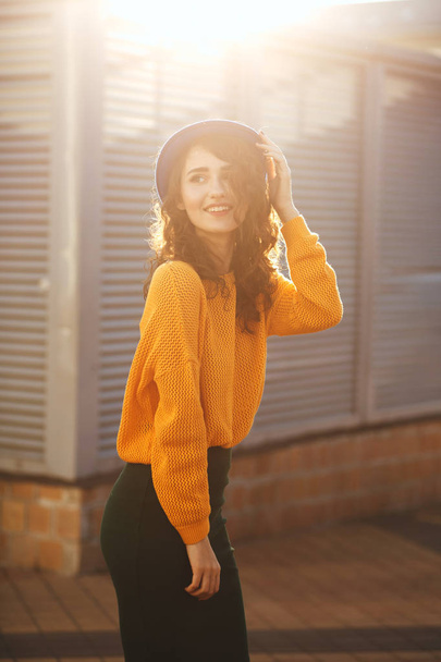 Lifestyle portrait of trendy dressed happy woman wearing blue hat and yellow sweater enjoying sunny evening - Photo, Image
