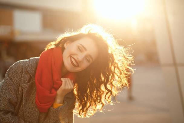 Lifestyleporträt einer fröhlichen brünetten Dame mit welligem Haar, die einen übergroßen Mantel und einen roten Schal trägt. Leere Räume - Foto, Bild