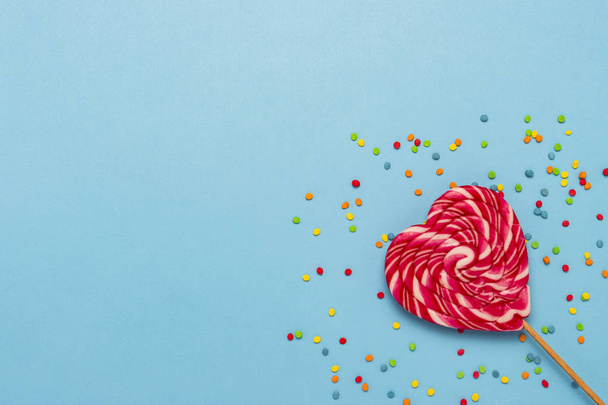 Pink lollipop in the shape of a heart and multicolored sweets on a blue background. Concept of sweets, love, a gift for a loved one. Flat lay, top view, copy space. - Photo, Image