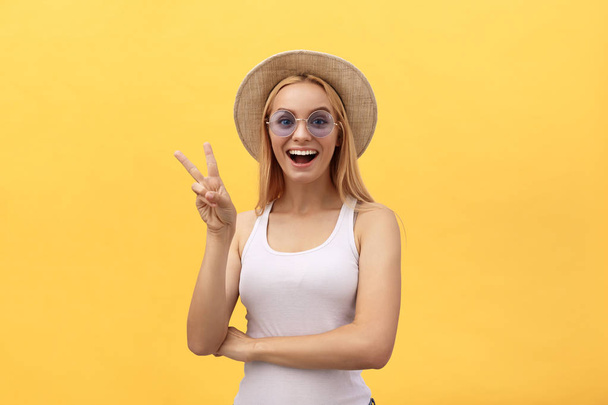 Kuva iloinen valkoihoinen nainen yllään rento vaatteet hymyilevä ja osoittaa rauhan merkki kaksi sormea eristetty keltaisella taustalla studiossa
. - Valokuva, kuva