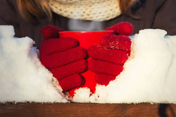 Руки женщины в красных перчатках держат красную чашку с горячим чаем. Зимняя концепция
.  - Фото, изображение