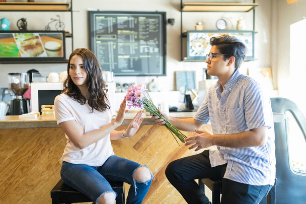 Sad young man offering flowers to angry partner while having a date in cafe - Photo, Image