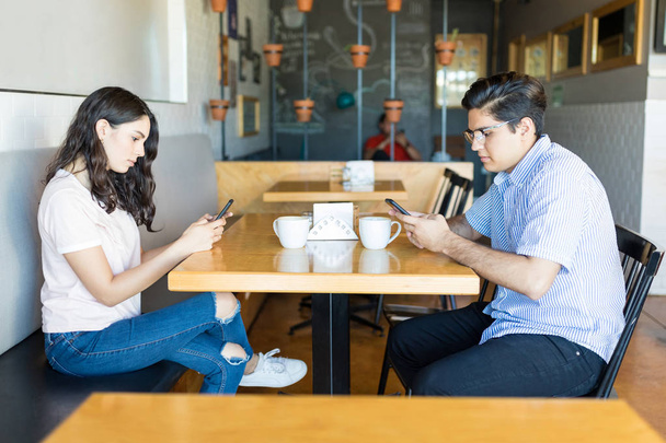 Грубые молодые партнеры используют смартфоны, пока тусуются в кафе
 - Фото, изображение