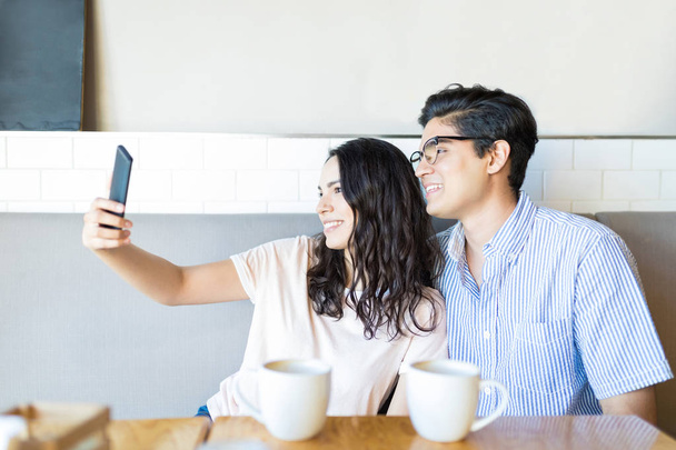 Happy boyfriend and girlfriend capturing memories on smartphone while hanging out in cafe - 写真・画像