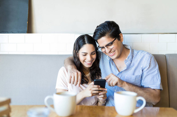 Szczęśliwy partnerzy oglądają śmieszne zdjęcia na telefon komórkowy podczas daty kawy - Zdjęcie, obraz