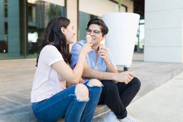 Cheerful loving woman feeding cone icecream to partner on a date in shopping mall - Photo, Image