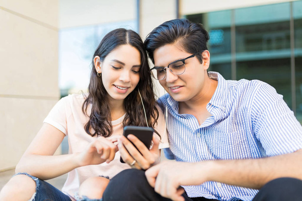 Young Hispanic couple listening to online music on smartphone at shopping mall - Photo, Image
