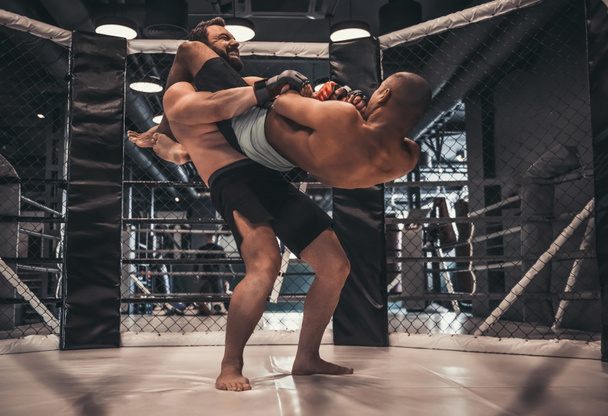 Two men in gloves and shorts are fighting in cage using grappling - Photo, Image