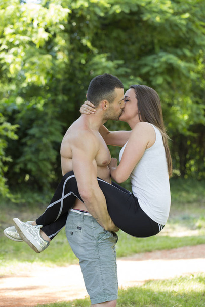 Молодая счастливая пара, мужчина и женщина занимаются спортом в парке. Они целуются в парке. Прекрасные, эмоциональные и романтические моменты
 - Фото, изображение