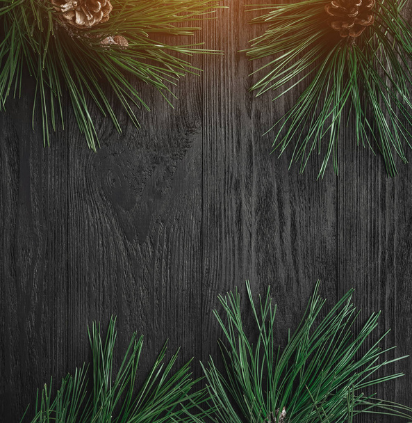 Рождественская открытка Фон из черного дерева с сосновыми ветвями и шишками через углы, вид сверху. Рождественская открытка. Эффект света
. - Фото, изображение