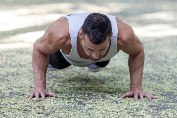 Picture of a young sportsman doing push ups outdoors, fitness and exercising in the park. Sport, recreation, lifestyle concept - Photo, Image