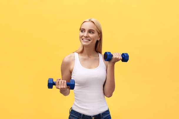 Mulher fitness levantando pesos sorrindo feliz isolado no fundo amarelo. ajuste desportivo caucasiano feminino modelo de fitness
 - Foto, Imagem