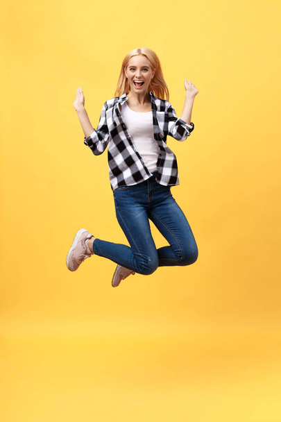Portrait of surprised young woman in black pants jumping in front of yellow wall. Indoor portrait of young lady in fooling around in studio - Foto, Imagem