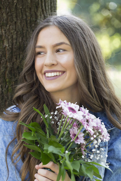 Young girl with a beautiful smile, holding a bouquet of flowers and enjoying the beautiful sunny summer / spring day - Foto, Imagem