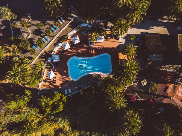 Отель Avida, Гран-Канария, Испания, 5 июля 2018 года. Вид с воздуха на бассейн на курорте у бара и пальм, расположенных в горах
. - Фото, изображение