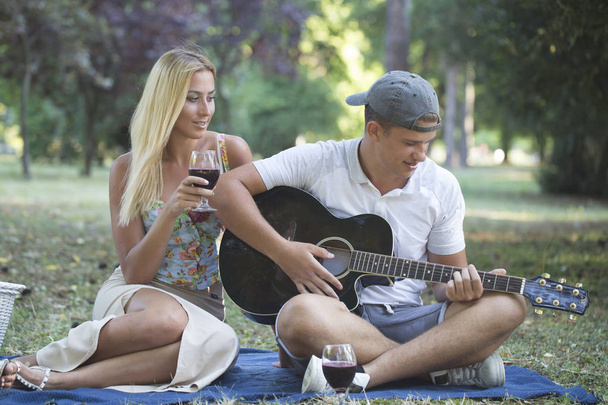 Young man playing guitar to his girl summer day couple love sitting green grass outdoor picnic nature guy  singing song - 写真・画像