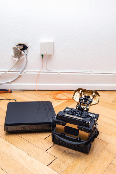 FTTH fiber installation at home with new arc clad-alignment fusion splicer used for splicing an array of thin optical fiber types with CATV on wall socket and tv internet receiver tuner vertical image - Photo, Image