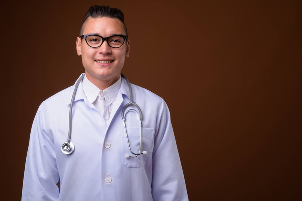 junger gutaussehender multi-ethnischer Arzt mit braunem Hintergrund - Foto, Bild