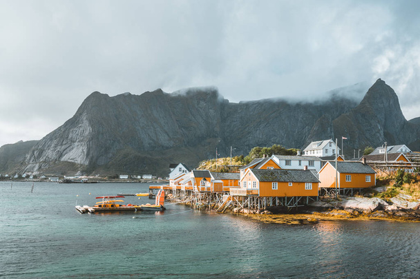 Yellow rorbu houses of Sakrisoy fishing village on a cloudy day with mountains in the background. Lofoten islands, Norway - Zdjęcie, obraz