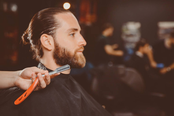 Közeli borotva kezében, fodrász, ügyfél háttér vár borotválkozás a szakáll és bajusz. - Fotó, kép