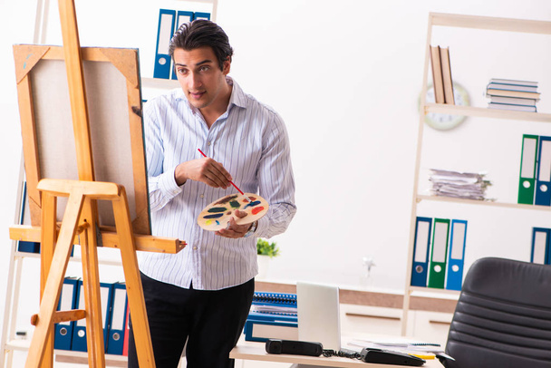 Joven empleado guapo disfrutando de la pintura en la oficina
  - Foto, Imagen