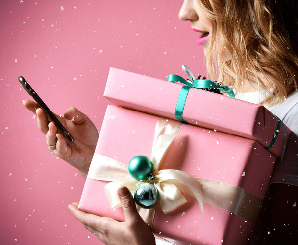 mujer de compras en línea con el teléfono móvil para Navidad presenta regalos sonriendo en rosa claro
 - Foto, imagen
