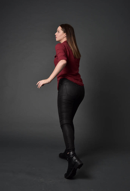 ritratto a figura intera di ragazza bruna che indossa camicia rossa e pantaloni di pelle. posa in piedi, su sfondo grigio studio
. - Foto, immagini