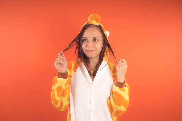pajamas in the form of a giraffe. emotional portrait of a girl on an orange background. crazy and funny woman in a suit. animator for childrens parties - Φωτογραφία, εικόνα