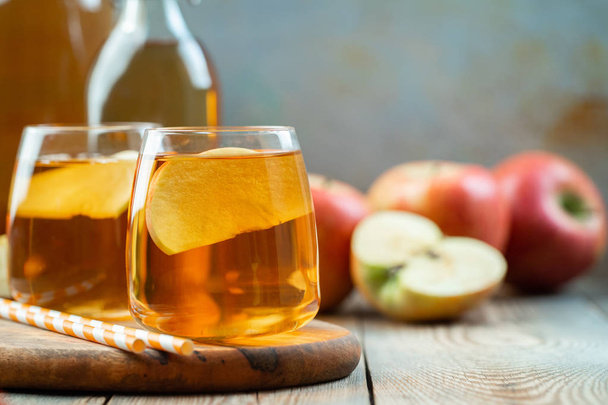 Οργανικό μηλόξυδο ή χυμό σε ένα ξύλινο τραπέζι με χώρο αντίγραφο. Δύο ποτήρια με ποτό και φθινόπωρο φύλλα σε ρουστίκ φόντο - Φωτογραφία, εικόνα