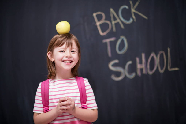 happy child holding apple on head with back to shool drawing on chalkboard in background - Fotografie, Obrázek