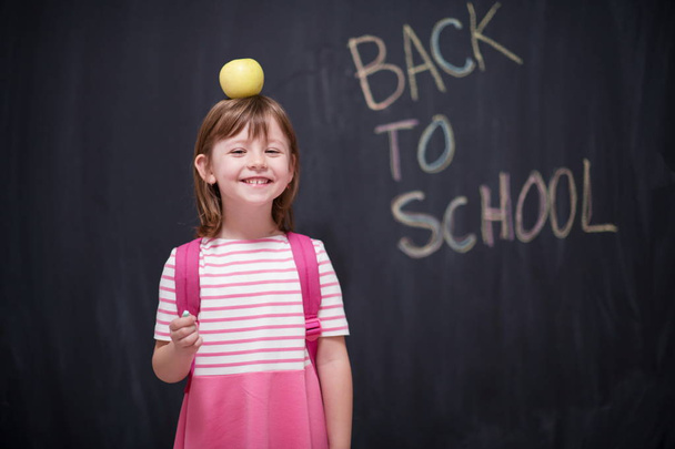 happy child holding apple on head with back to shool drawing on chalkboard in background - Фото, зображення