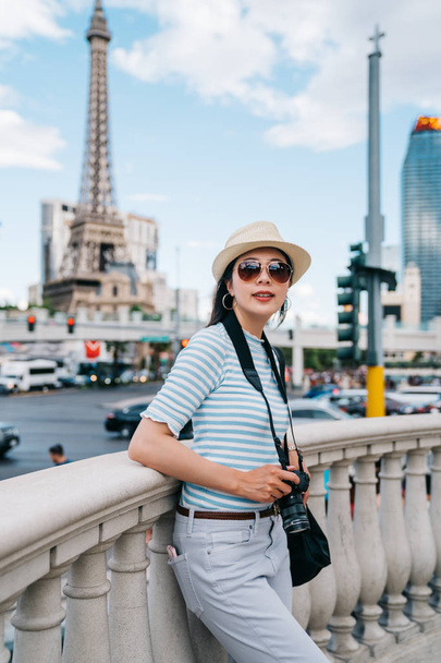 tourist taking picture with and confident smile, with tower in the background. young photographer standing outside hotel in las vegas. pretty girl join tourist tour in USA. - Foto, imagen
