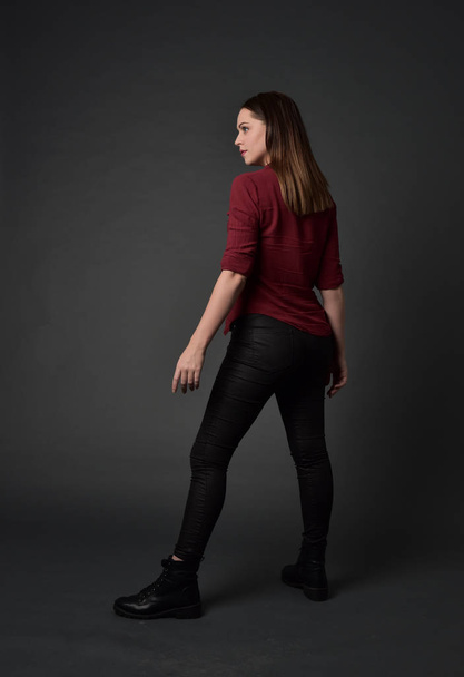 full length portrait of brunette girl wearing  red shirt and leather pants. standing pose , on grey studio background. - Fotoğraf, Görsel
