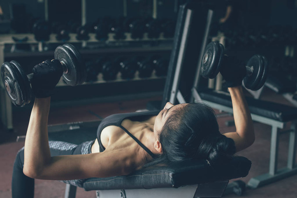 Beautiful asian woman lifting weights dumbbell for her chest near window at gym inside. - 写真・画像
