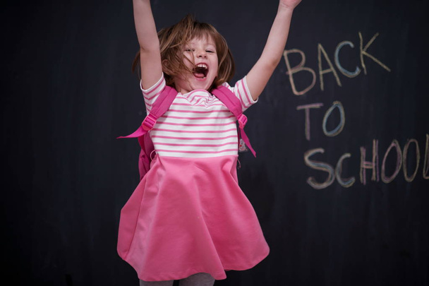 Happy school girl child with backpack writing  back to school on black chalkboard - Photo, Image