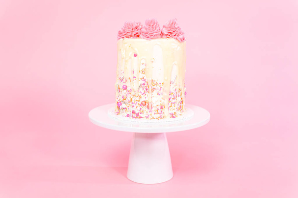 Rózsaszín és fehér vajkrém krém torta rózsaszín sprinkles és csepegtető fehér csokoládé ganache. - Fotó, kép