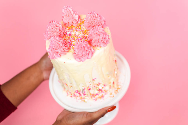 Kobieta trzyma różowy i biały lukier krem ciasto z różowy kropi i białym ganache czekolady kapać. - Zdjęcie, obraz