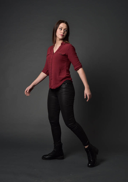 po celé délce portrét bruneta dívka, která nosí červené košile a kožené kalhoty. stojící pozice, na pozadí šedé studio. - Fotografie, Obrázek