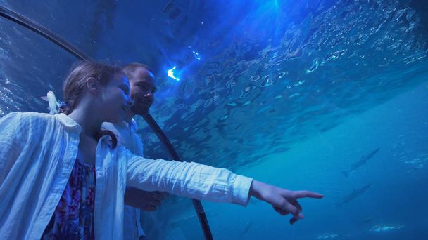Teini-ikäinen tyttö isän kanssa huvittavasti katsomassa kalaa akvaariossa
 - Valokuva, kuva