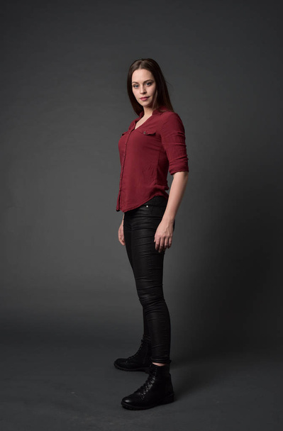 full length portrait of brunette girl wearing  red shirt and leather pants. standing pose , on grey studio background. - Foto, imagen