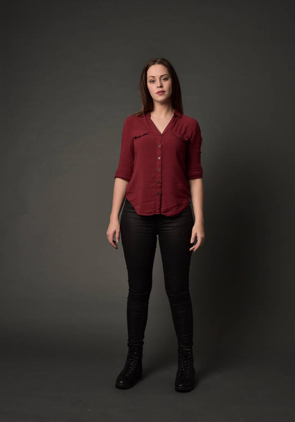 full length portrait of brunette girl wearing  red shirt and leather pants. standing pose , on grey studio background. - Photo, image