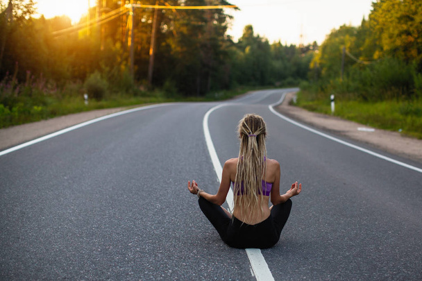 Mujer yoga medita sentada en medio del camino del campo
.  - Foto, imagen