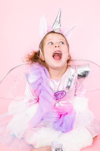 Portrait of a little girl in glitter unicorn costume on pink background. - Foto, immagini
