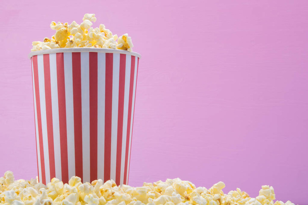 a bucket of popcorn stands on cereal, on a pink background, on the right there is a place to write - Фото, изображение