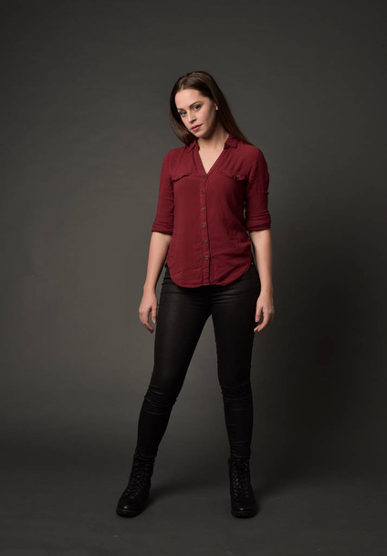 full length portrait of brunette girl wearing  red shirt and leather pants. standing pose , on grey studio background. - Valokuva, kuva