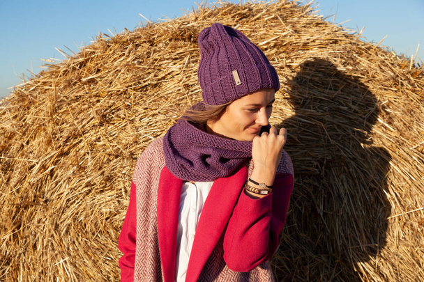 The concept of livestyle  outdoor in autumn. Close up of a young woman student in a warm autumn clothes looking funny, smilling, posing for the camera  around haystick - Фото, изображение
